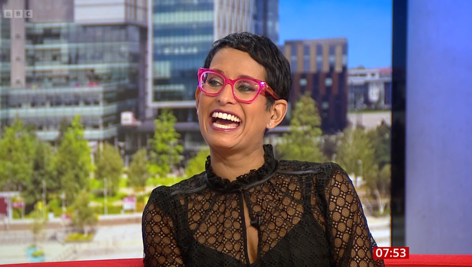 a woman wearing pink glasses and a black top is laughing and the time is 07:53