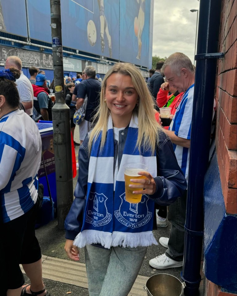 a woman wearing an everton scarf holds a glass of beer