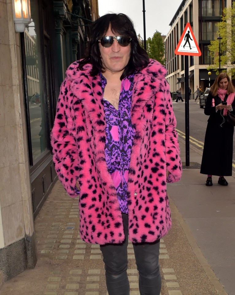 a man in a pink leopard print coat stands in front of a pedestrian crossing sign