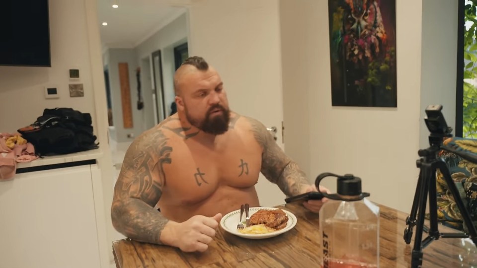 a man with tattoos on his chest is sitting at a table with a plate of food