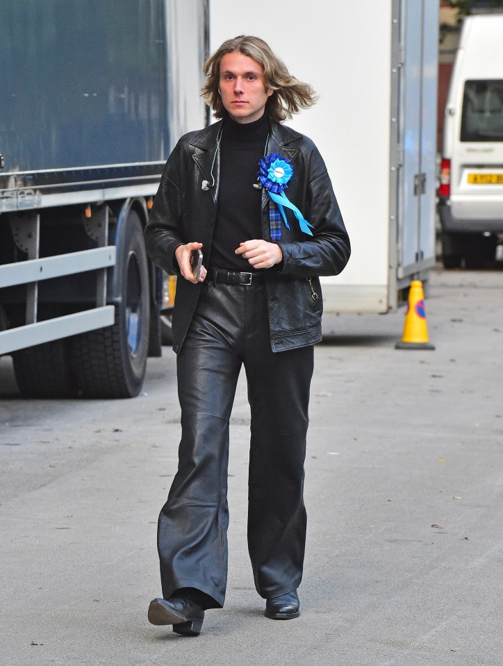 a man wearing a leather jacket has a blue flower pinned to his jacket