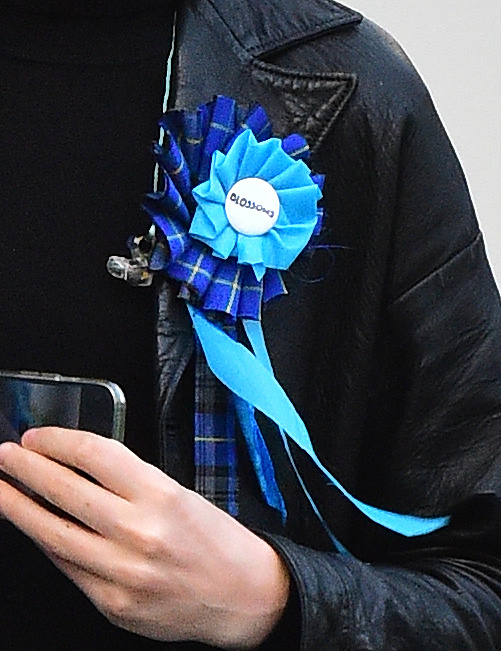 a person wearing a blue rosette with a button that says ' bloom ' on it