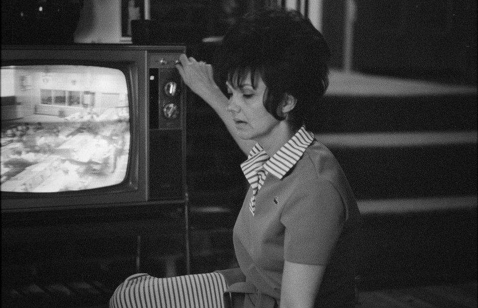 a black and white photo of a woman sitting in front of a television