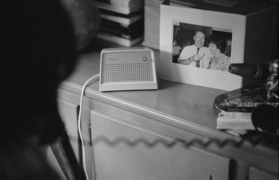 a black and white photo of a man and woman sits next to a crown radio