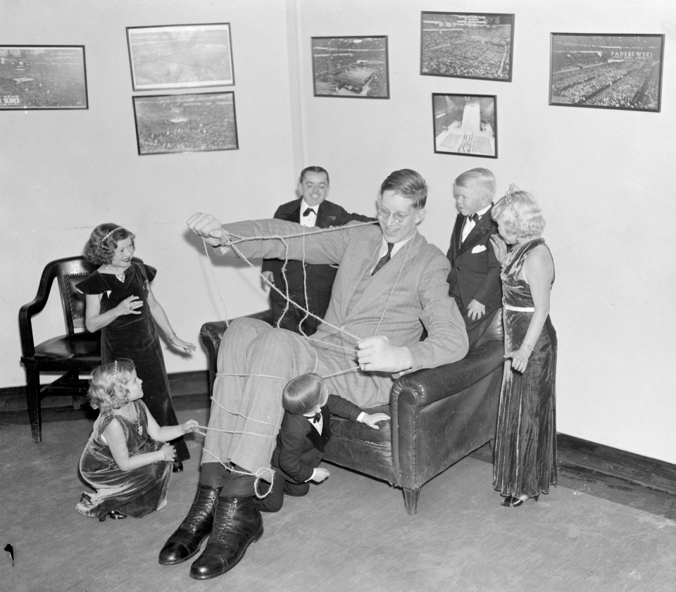 a black and white photo of a man sitting in a chair surrounded by children