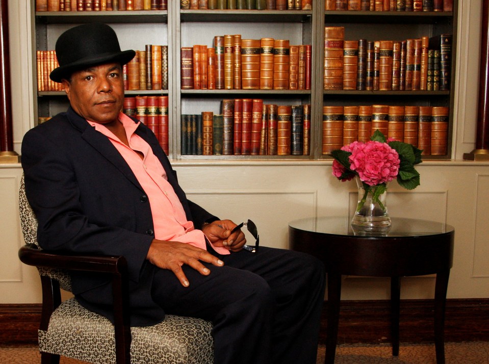 a man wearing a top hat sits in front of a bookshelf