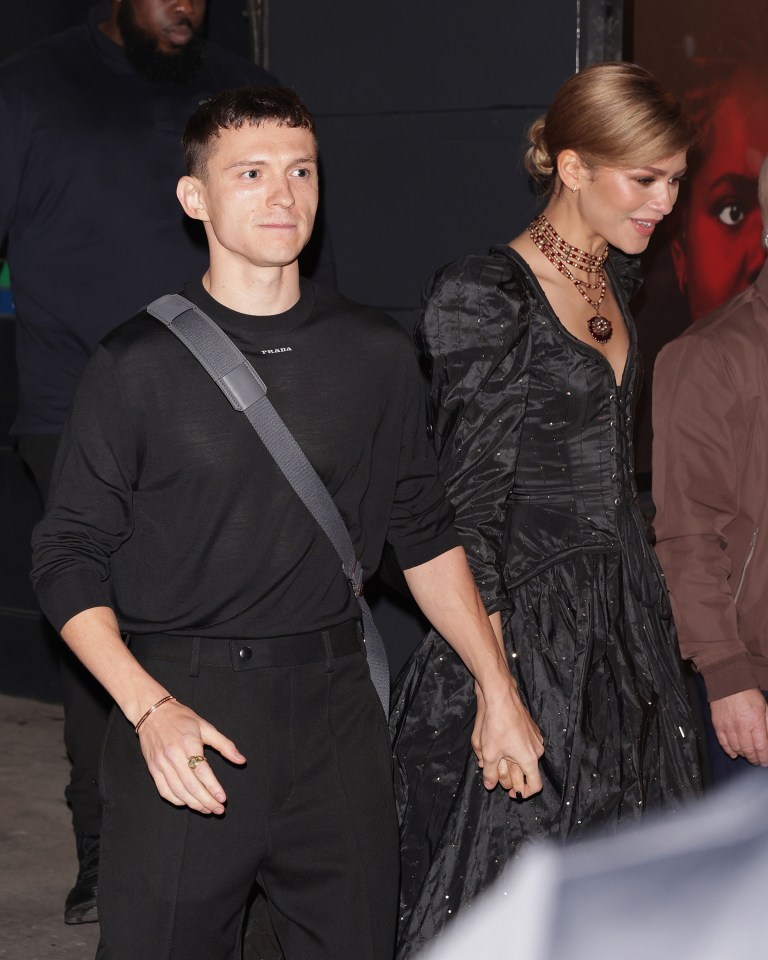 a man in a black prada shirt holds hands with a woman in a black dress