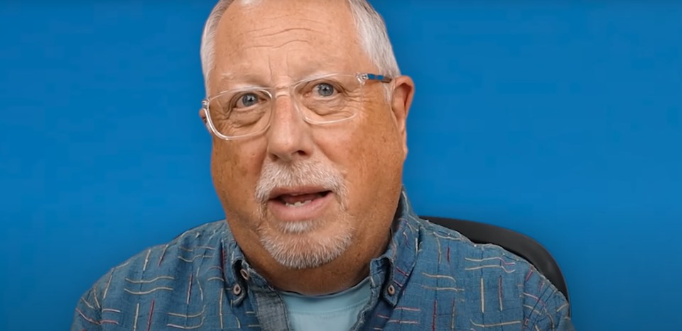 a man with glasses and a beard is sitting in front of a blue background