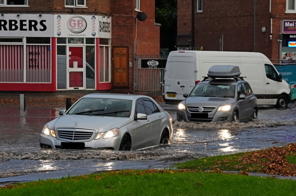 cars are driving through a flooded street in front of a barbers shop