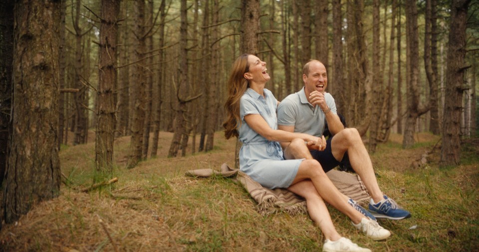 a man and woman sit on a blanket in the woods laughing