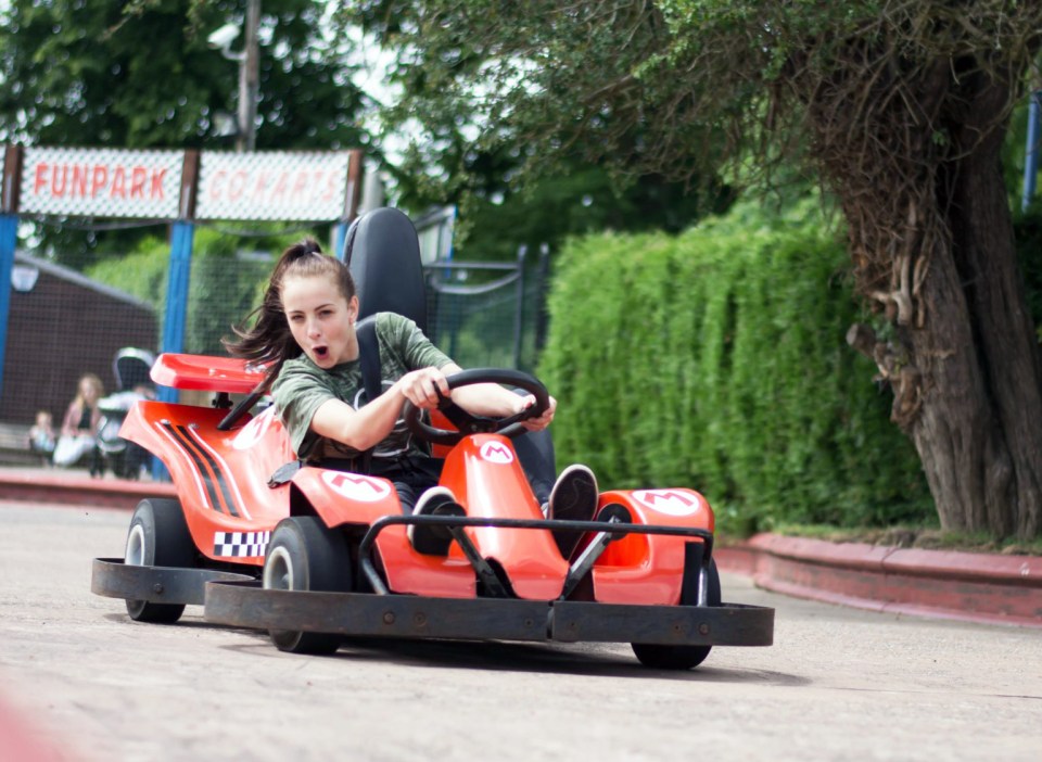 a girl driving a go kart in front of a sign that says funpark