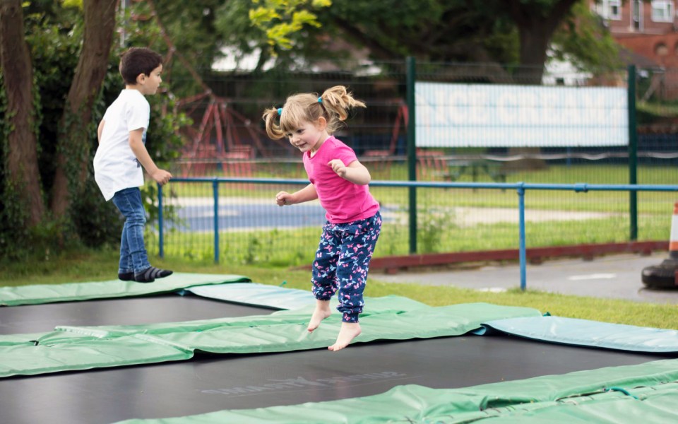 a little girl in a pink shirt is jumping on a trampoline