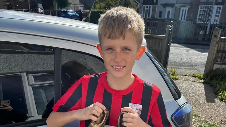 a young boy in a red and black striped shirt is standing in front of a car .