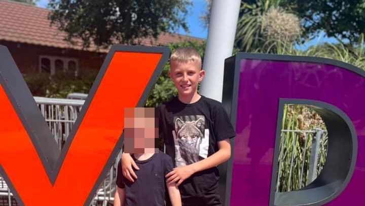 two young boys are standing next to each other in front of a large purple sign .