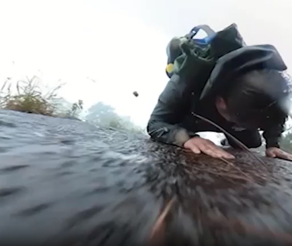 a man with a backpack is crawling on a rock in the water .