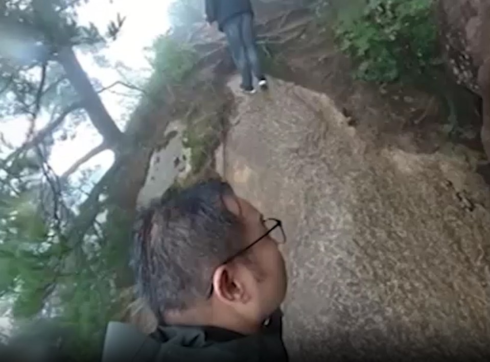 a man wearing glasses is standing on a rock in the woods