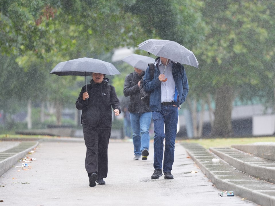 three people walking in the rain with umbrellas one of whom is wearing a jacket that says fila