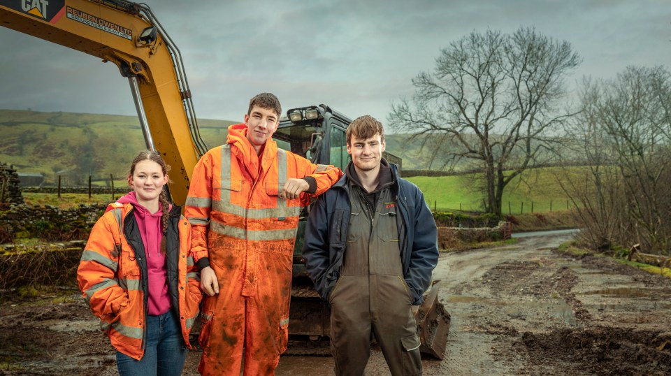 three people standing in front of a yellow cat excavator