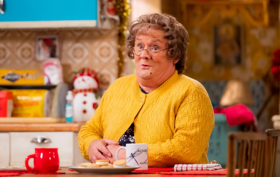 a woman in a yellow sweater sits at a table with a mug that says agnes