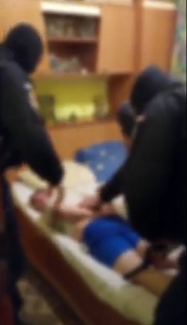 a group of people are standing around a man laying on a bed .