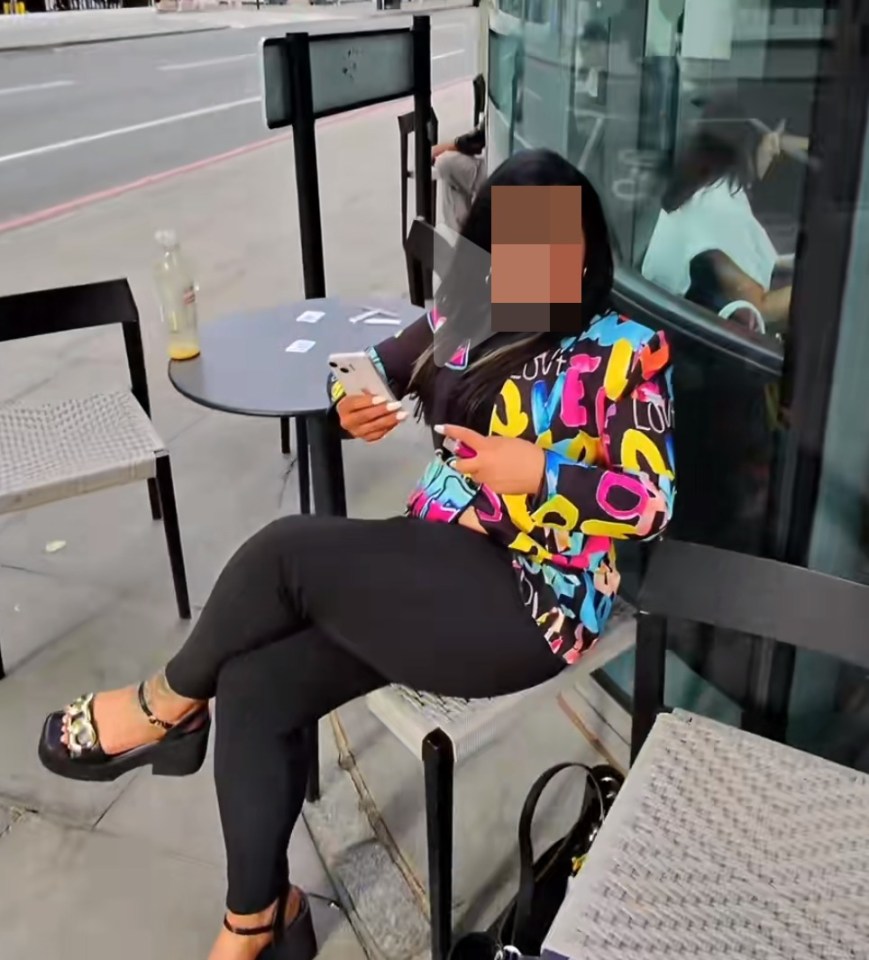 a phone screen shows a woman sitting at a table with her legs crossed