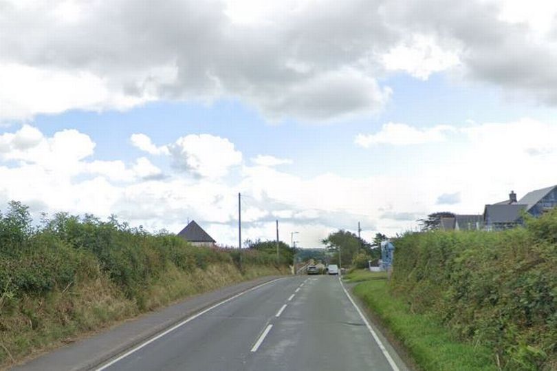 a car is driving down a country road on a cloudy day .