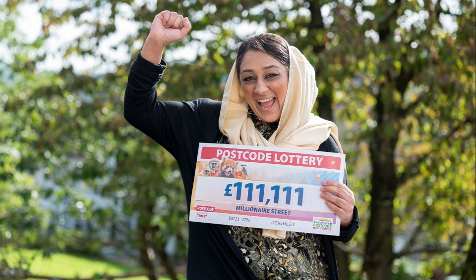 a woman holds up a postcode lottery ticket