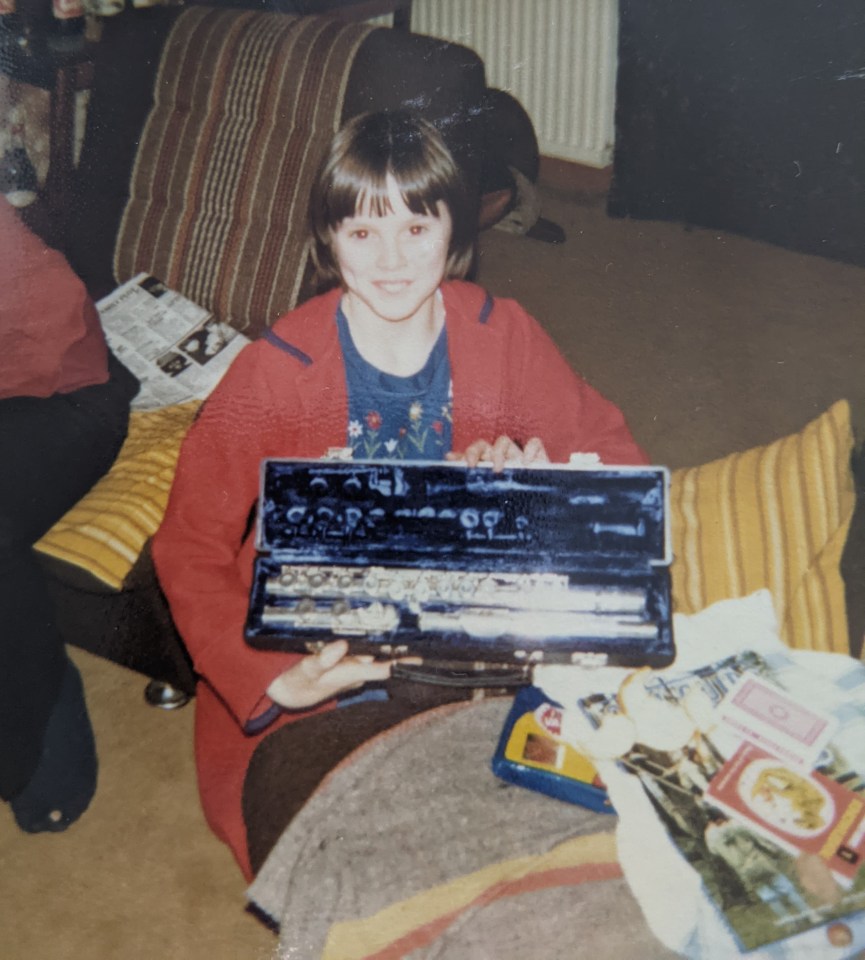 a young girl in a red jacket is holding a flute case