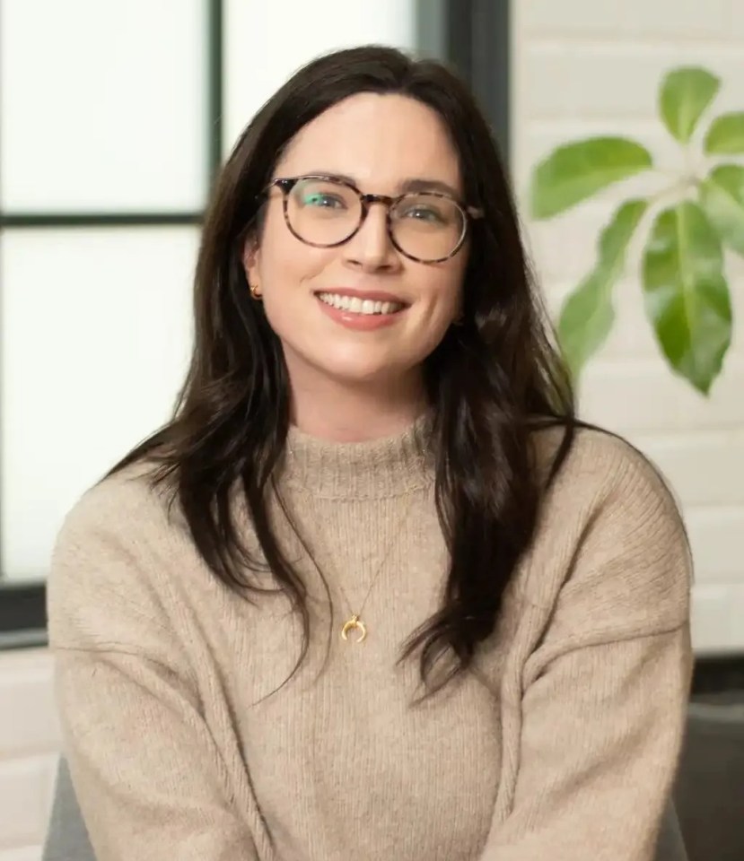 a woman wearing glasses and a sweater is smiling for the camera .