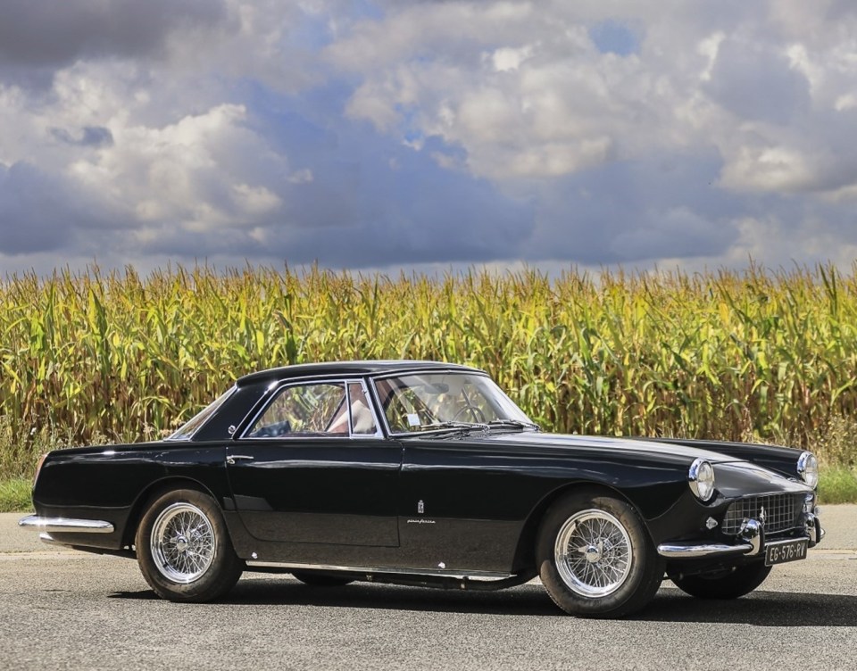 a black car is parked in front of a field of corn