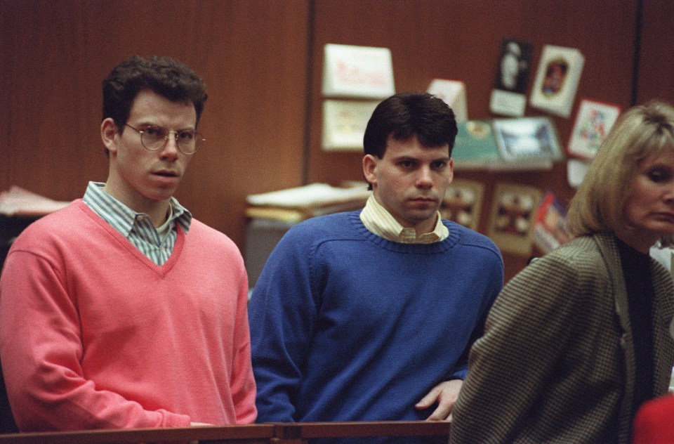 a man in a pink sweater stands next to another man in a blue sweater