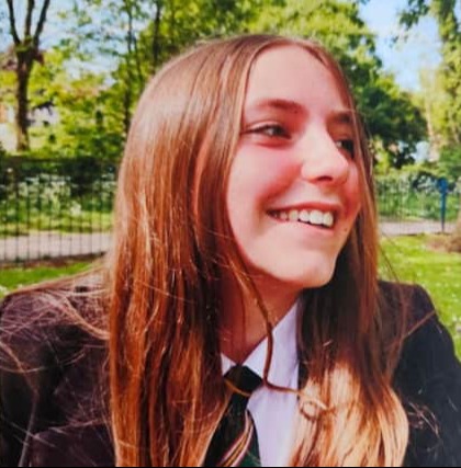 a young girl in a school uniform is smiling in a park .