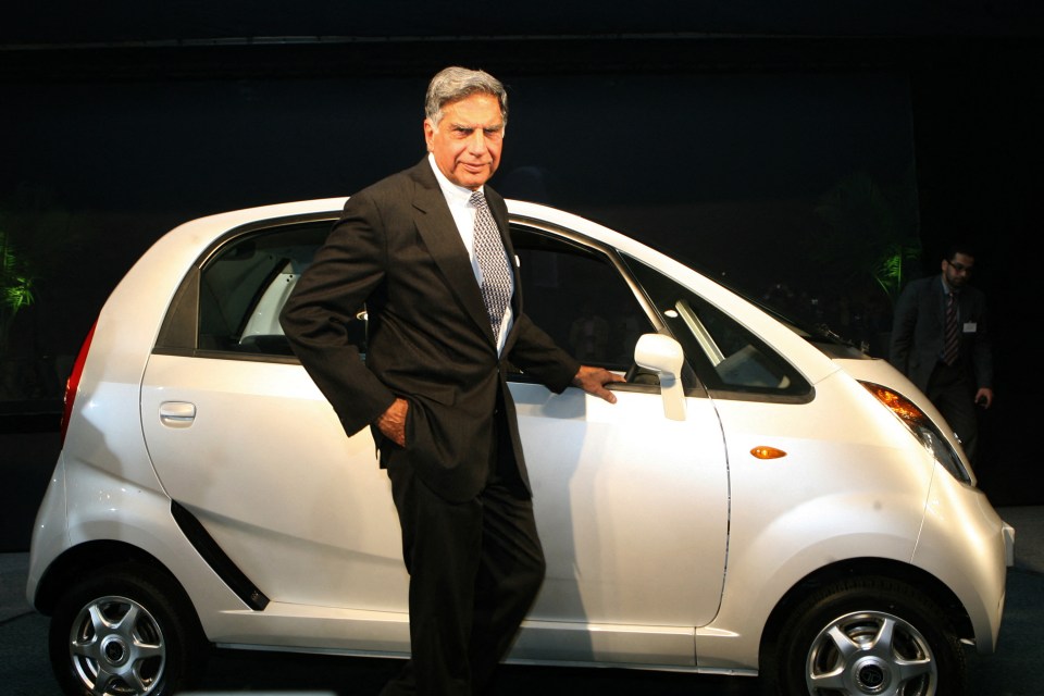 a man in a suit stands next to a small white car