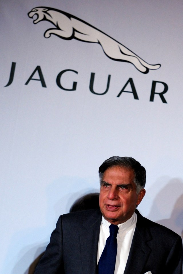 a man in a suit and tie stands in front of a jaguar logo