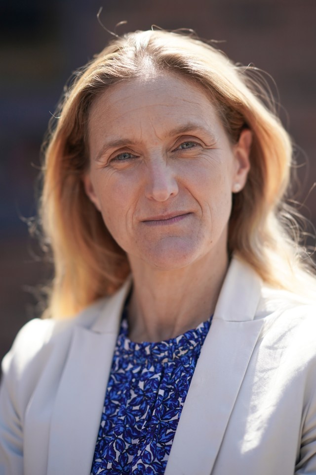 a woman wearing a white jacket and a blue shirt looks at the camera