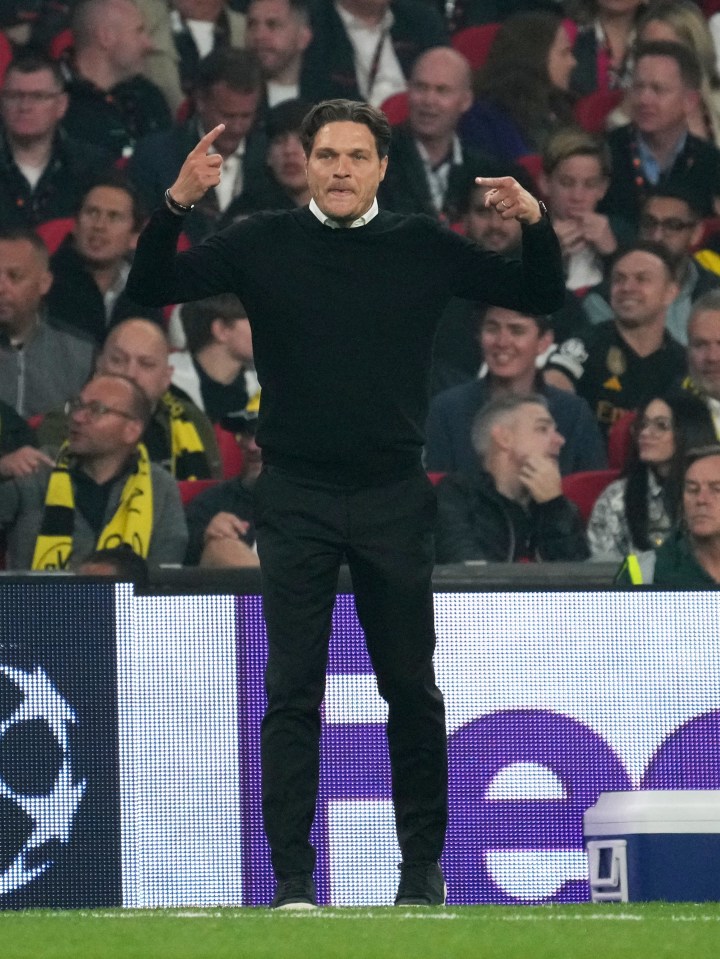 a man in a black sweater stands on a soccer field