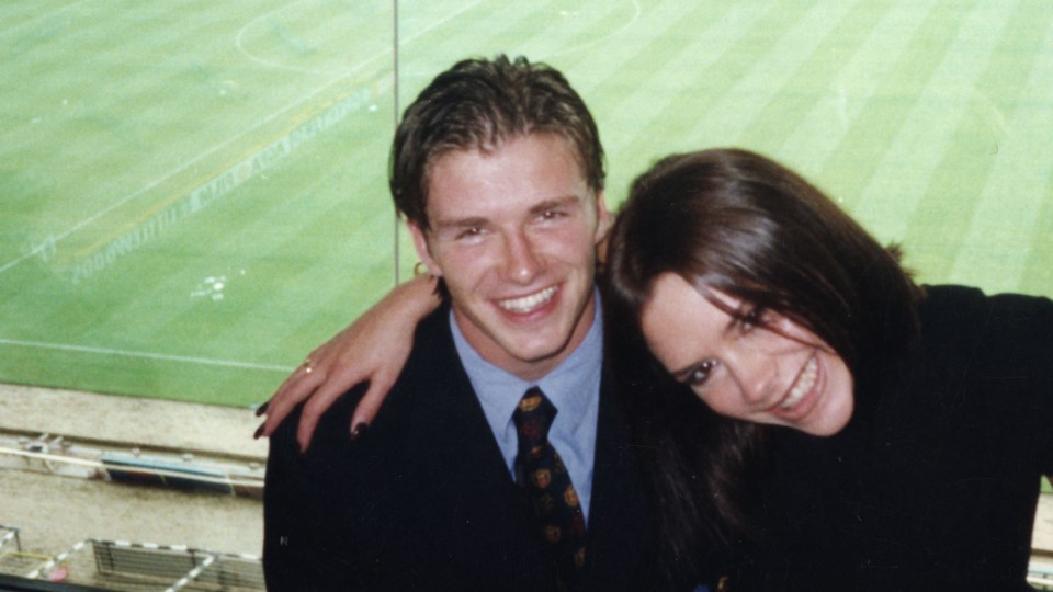 a man and woman are posing for a picture in front of a soccer field