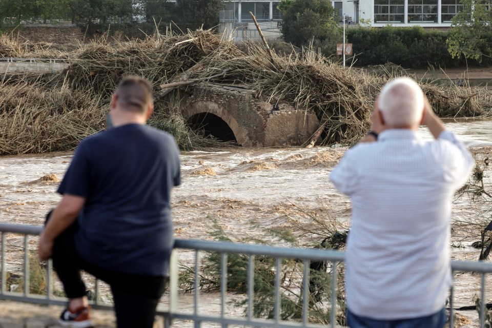 Residents take pictures of a damaged bridge in the flood-hit municipality of Ribarroja del Turia, in the province of Valencia