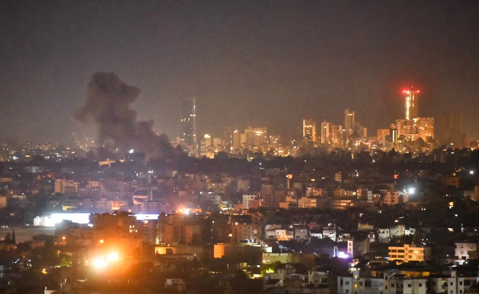 a city at night with smoke coming out of the sky