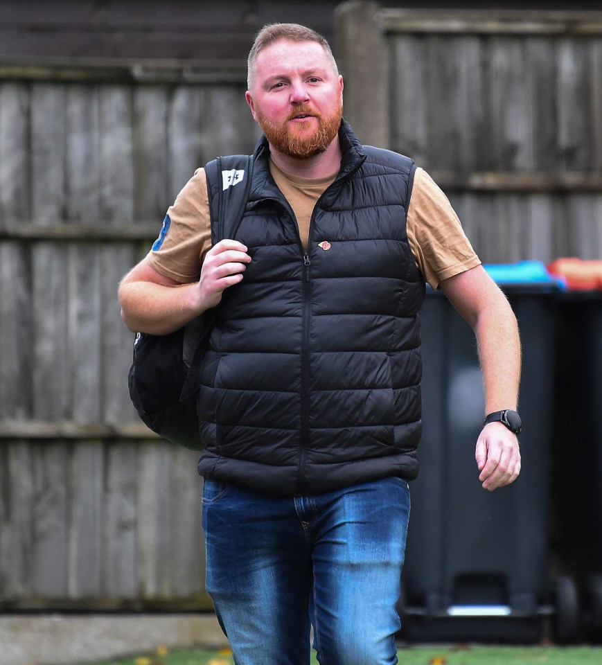 a man with a beard wearing a black vest and carrying a bag