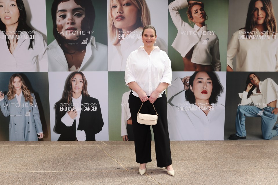 a woman stands in front of a wall of posters that say witchery