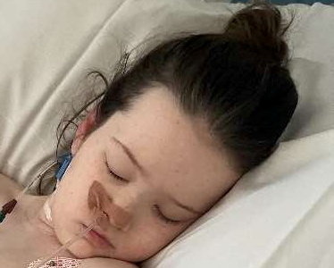 a young girl is sleeping in a hospital bed with a tube in her nose .