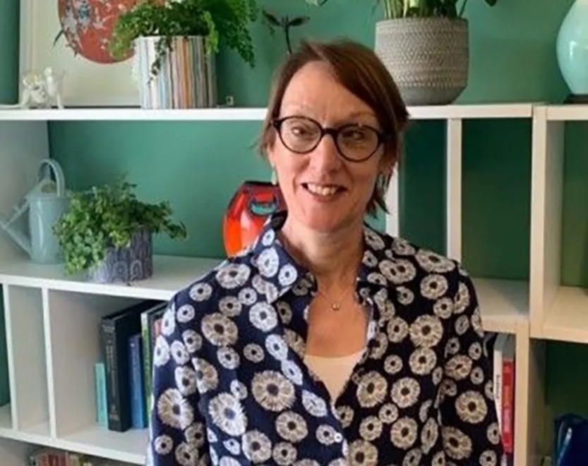 a woman wearing glasses is standing in front of a bookshelf filled with potted plants .