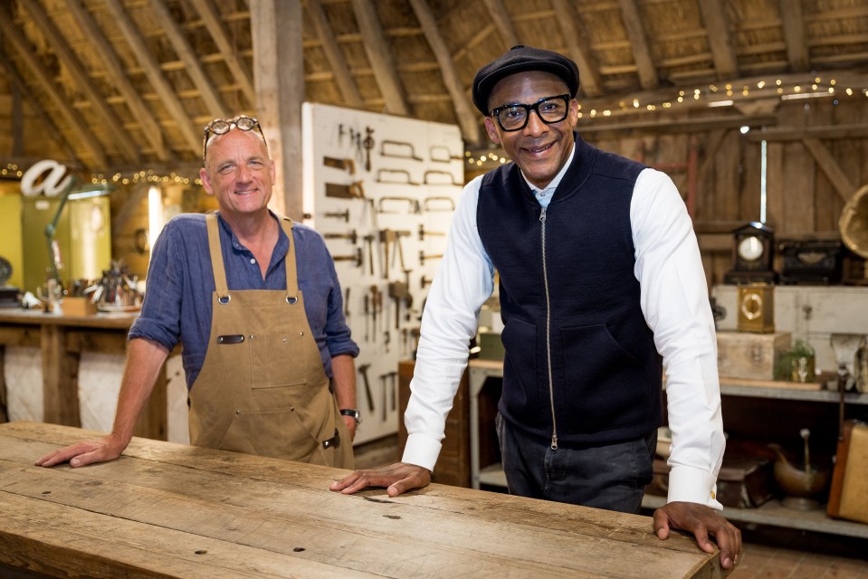 two men standing next to each other in front of a wall with tools on it