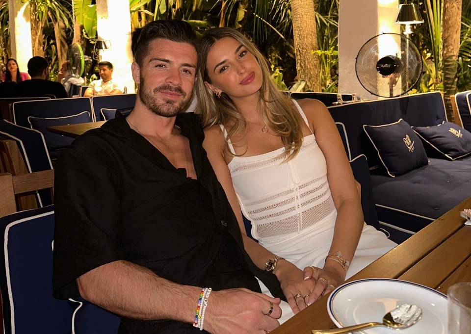 a man and a woman are sitting at a table with a fan in the background