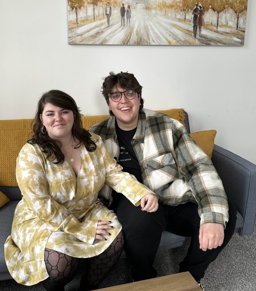 a man and a woman sit on a couch in front of a painting of the eiffel tower