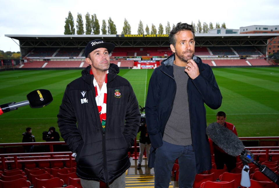 two men stand in front of a stadium with a yellow sign that says wrexham lager stand