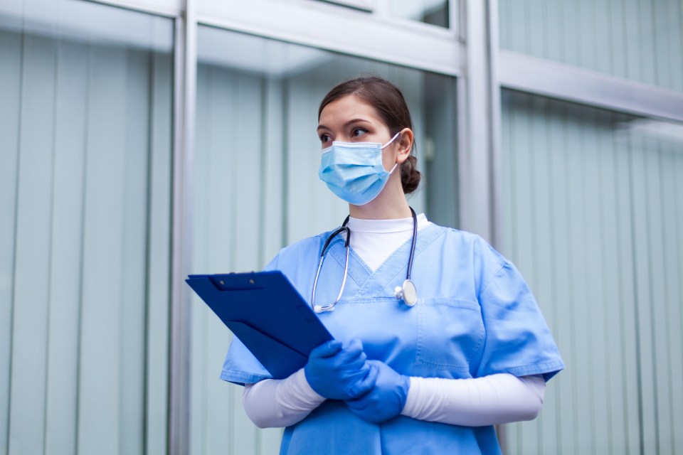 a nurse wearing a mask and gloves holds a clipboard