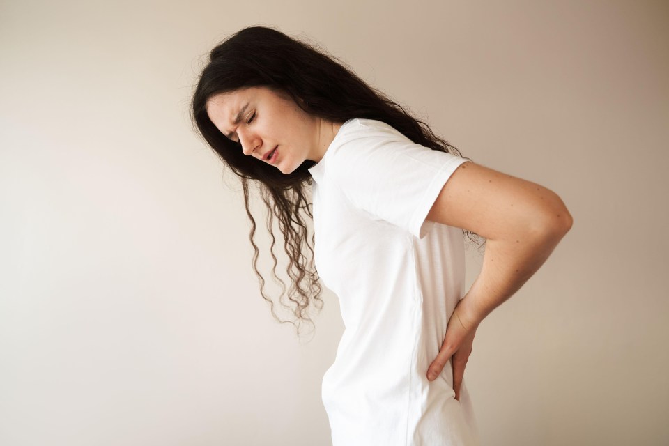 a woman in a white t-shirt is holding her back in pain