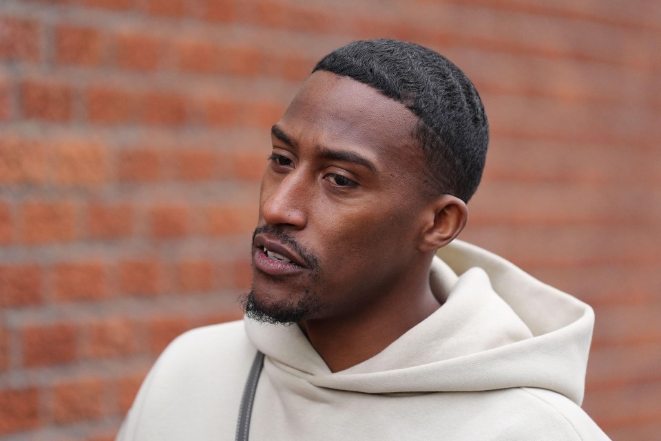 a man wearing a white hoodie stands in front of a brick wall